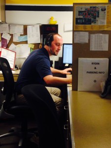 Adam Shreiber, Campus Safety Operations Supervisor, working the front desk of Campus Safety Headquarters in lower level Harstad.